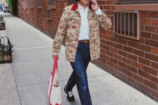 close-up of a man wearing a patterned chore coat with dark blue jeans, carrying a tote bag and talking on the phone