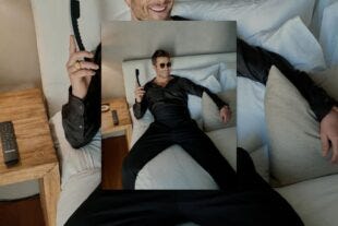 glen powell lounging on a bed in formalwear, holding a phone, wearing sunglasses, and smiling