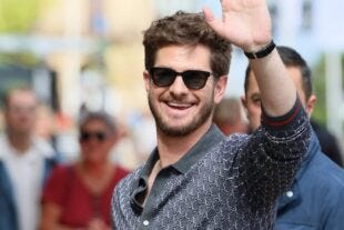 close-up of the actor andrew garfield, smiling and waving while wearing sunglasses